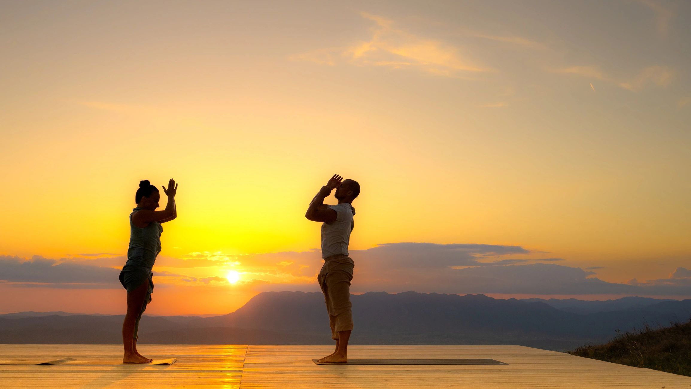 Two people practicing yoga outdoors at sunrise in the mountains