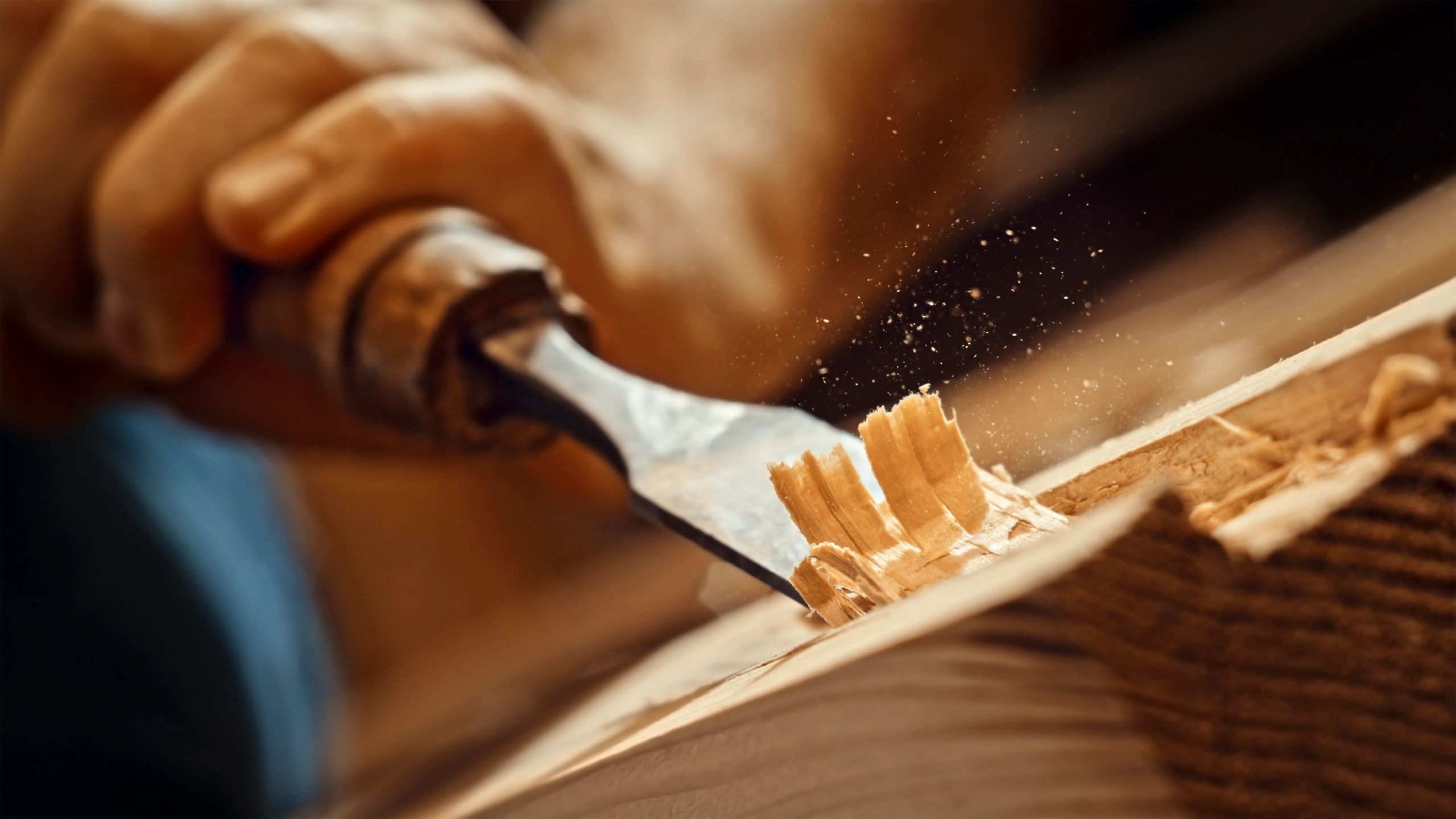 Hand using a chisel to shape wood in a workshop